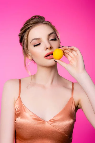 Elegant beautiful blonde woman with closed eyes in silk dress holding apricot isolated on pink — Stock Photo