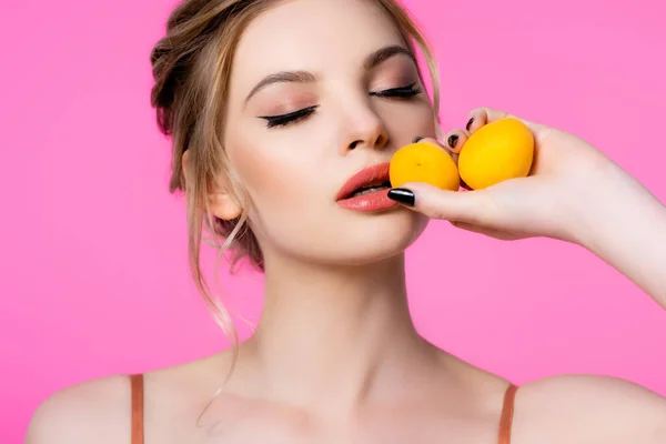 Elegant beautiful blonde woman with closed eyes holding apricots isolated on pink — Stock Photo