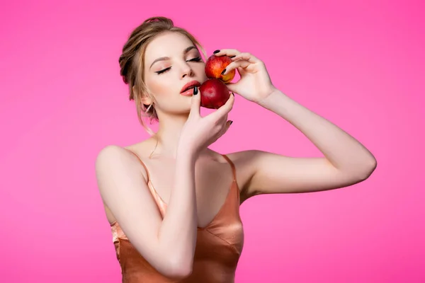 Elegante schöne blonde Frau im Seidenkleid mit geschlossenen Augen hält Pfirsiche isoliert auf rosa — Stockfoto
