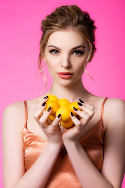 Elegant beautiful blonde woman in silk dress holding ripe apricots isolated on pink — Stock Photo
