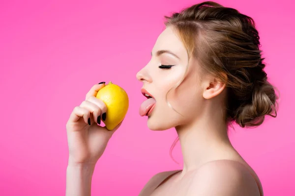 Vue latérale de belle femme blonde élégante léchant citron mûr isolé sur rose — Photo de stock