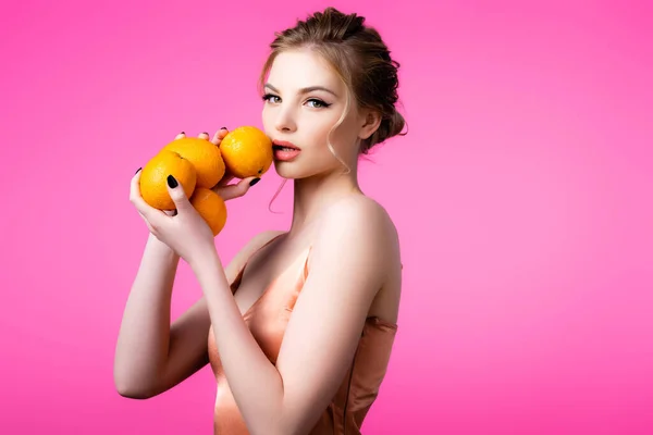 Elegante hermosa mujer rubia sosteniendo naranjas maduras aisladas en rosa - foto de stock