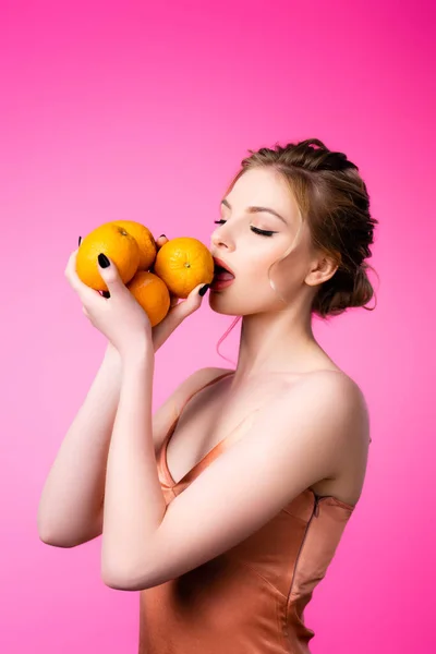 Elegant beautiful blonde woman licking ripe oranges isolated on pink — Stock Photo