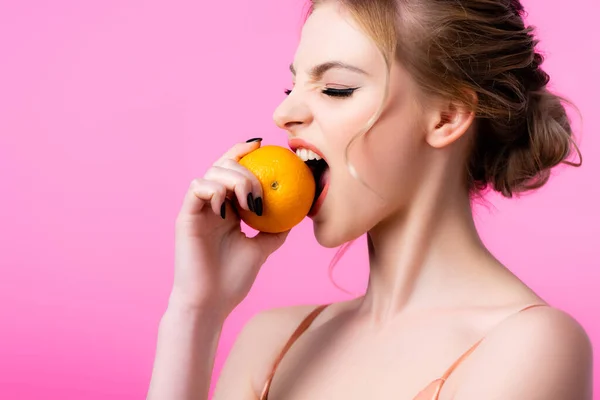 Hermosa mujer rubia mordiendo naranja madura aislado en rosa - foto de stock