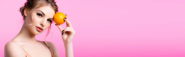 Elegant beautiful blonde woman holding ripe orange isolated on pink, panoramic shot — Stock Photo