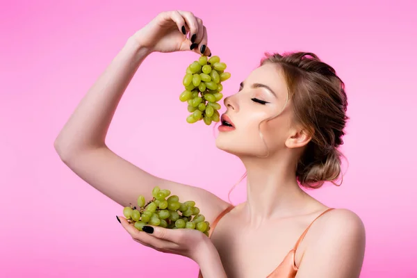 Elegant beautiful blonde woman holding green grapes near mouth isolated on pink — Stock Photo