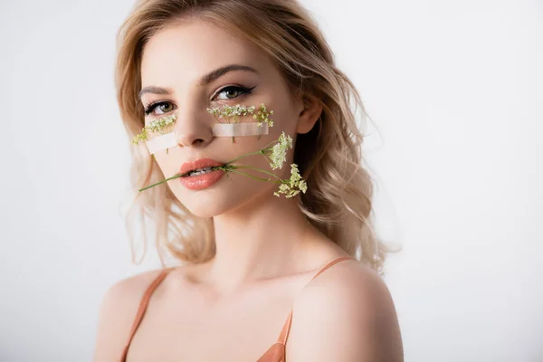 Beautiful blonde woman in silk dress with wildflowers under eyes and in mouth isolated on white — Stock Photo
