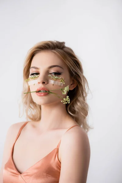 Beautiful blonde woman in silk dress with wildflowers under eyes and in mouth isolated on white — Stock Photo