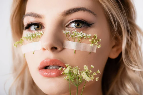 Schöne blonde Frau mit Wildblumen unter den Augen und im Mund isoliert auf weiß — Stockfoto
