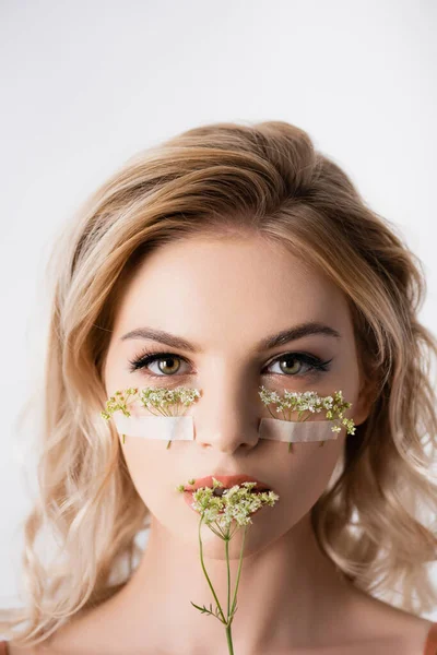 Belle femme blonde avec des fleurs sauvages sous les yeux et près de la bouche isolé sur blanc — Photo de stock