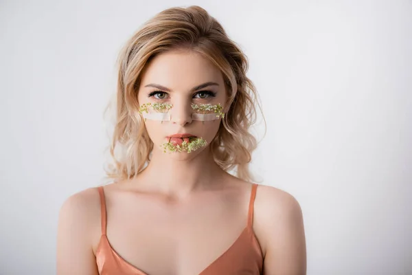 Beautiful blonde woman in silk dress with wildflowers under eyes and in mouth isolated on white — Stock Photo