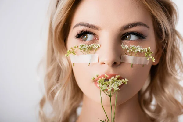 Schöne blonde Frau mit Wildblumen unter Augen und in der Nähe Mund isoliert auf weiß — Stockfoto