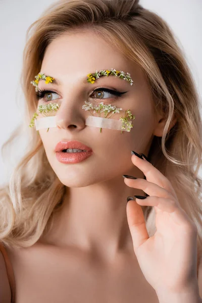 Bella donna bionda con fiori di campo sotto gli occhi guardando lontano isolato su bianco — Foto stock