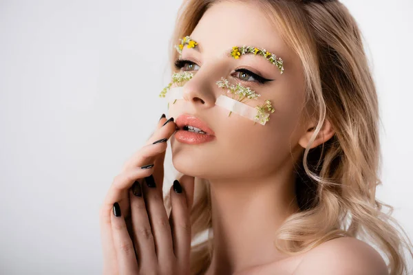 Naked beautiful blonde woman with wildflowers under eyes touching face isolated on white — Stock Photo