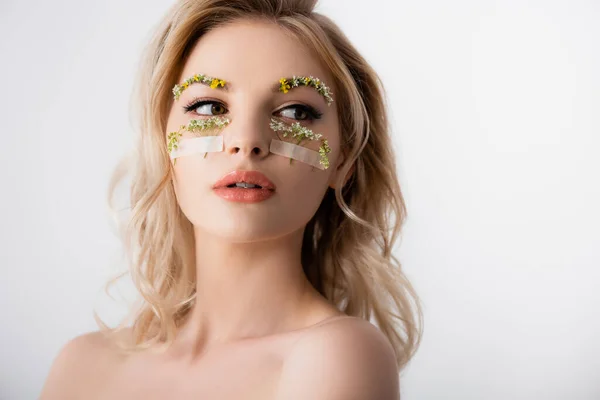 Nackte schöne blonde Frau mit Wildblumen unter den Augen, die isoliert auf weiß wegschauen — Stockfoto