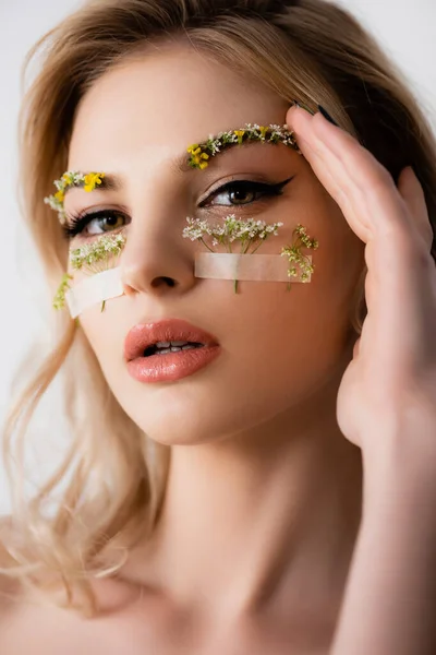 Nackte schöne blonde Frau mit Wildblumen unter Augen und Hand in der Nähe Gesicht isoliert auf weiß — Stockfoto