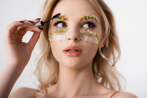 Beautiful blonde woman styling wildflowers on eyebrows with brow gel isolated on white — Stock Photo