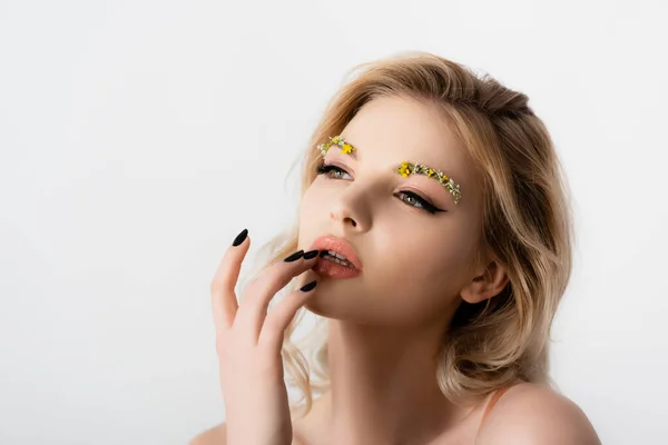 Beautiful blonde woman with wildflowers on eyebrows touching lips isolated on white — Stock Photo