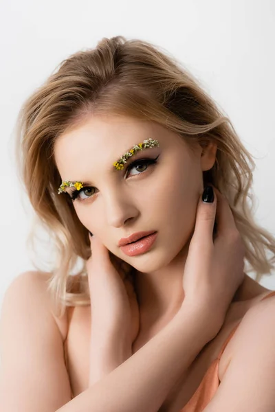 Beautiful blonde woman with wildflowers on eyebrows touching neck isolated on white — Stock Photo