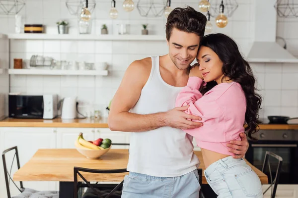 Uomo sorridente abbracciando bella fidanzata in cucina — Foto stock