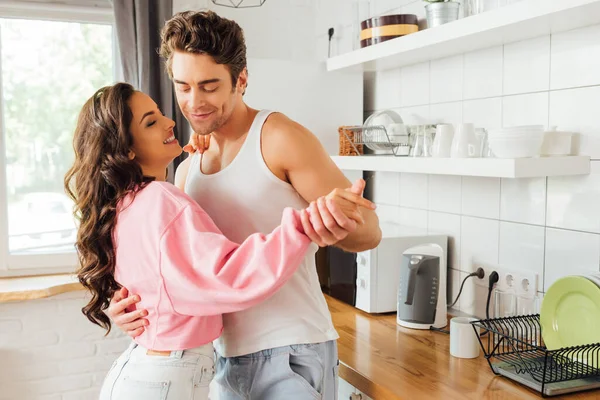 Sorridente giovane uomo che balla con bella ragazza in cucina — Foto stock