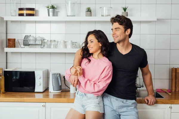 Smiling man embracing beautiful woman near worktop in kitchen at home — Stock Photo