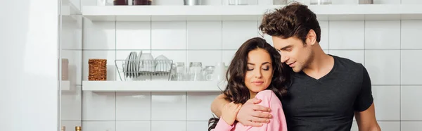 Tiro panorâmico de homem bonito abraçando mulher bonita na cozinha — Fotografia de Stock