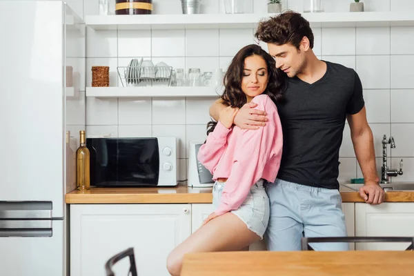 Foco seletivo de homem bonito abraçando namorada sexy na cozinha em casa — Fotografia de Stock