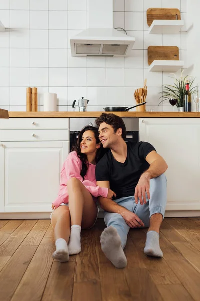 Selective focus of smiling young couple sitting on floor in kitchen — Stock Photo