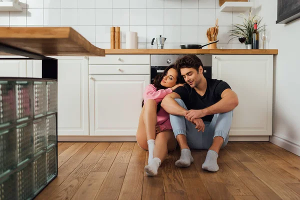 Enfoque selectivo de la hermosa mujer abrazando novio con los ojos cerrados en el piso de la cocina - foto de stock