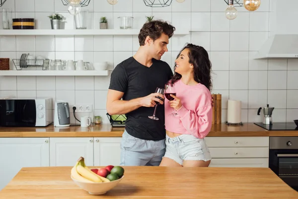 Foco seletivo de sorrir menina clinking vinho com namorado bonito na cozinha — Fotografia de Stock