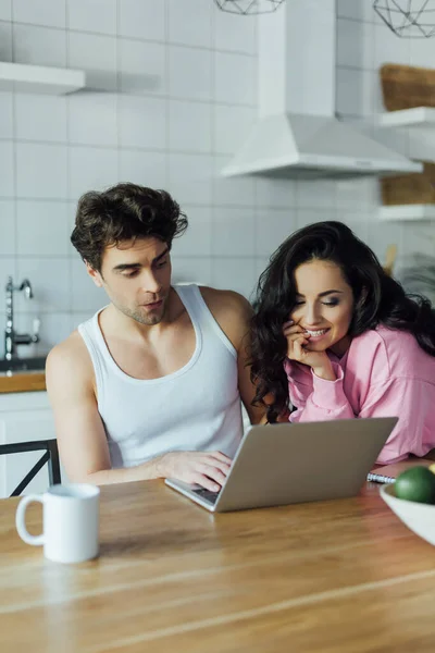 Selektiver Fokus einer lächelnden Frau, die in der Küche neben ihrem Freund auf den Laptop schaut — Stockfoto