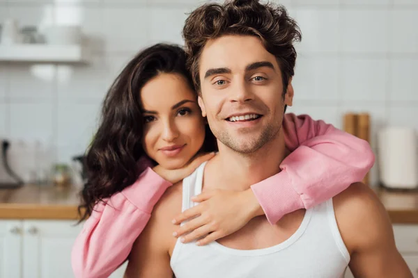 Beautiful woman embracing smiling man and looking at camera at home — Stock Photo