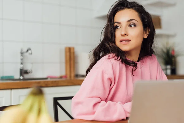 Selektiver Fokus der schönen Frau, die in der Nähe des Laptops in der Küche wegschaut — Stockfoto