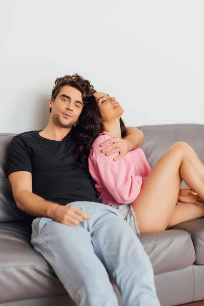 Enfoque selectivo del hombre guapo abrazando a la hermosa mujer en el sofá sobre fondo gris - foto de stock