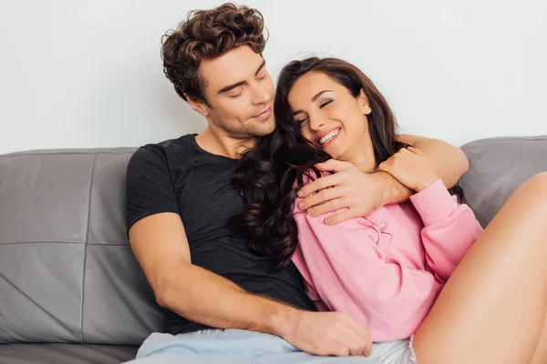 Selective focus of smiling woman touching boyfriend on sofa on grey background — Stock Photo