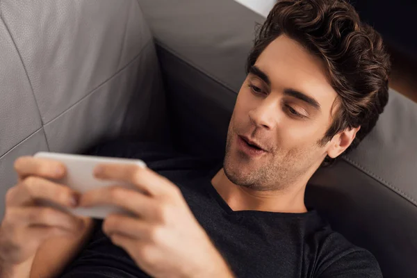 Selective focus of excited man using smartphone on couch — Stock Photo