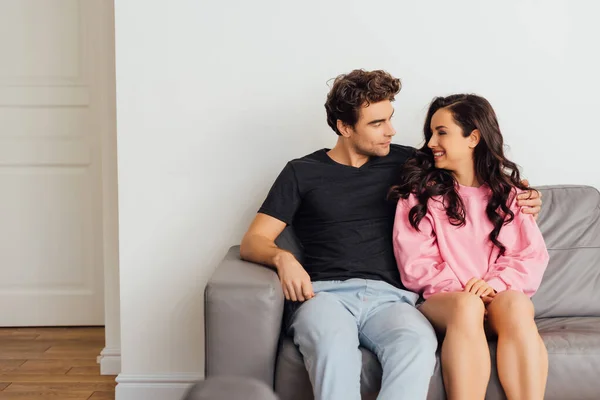 Selective focus of handsome young man hugging smiling woman on sofa in living room — Stock Photo
