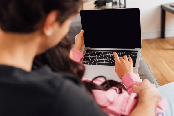 Concentration sélective des jeunes couples utilisant un ordinateur portable ensemble sur le canapé à la maison — Photo de stock