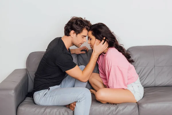 Боковой вид красивого мужчины трогательное лицо красивой девушки на диване на сером фоне — стоковое фото