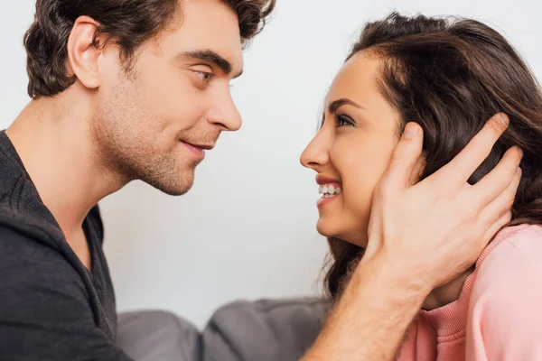 Schöner Mann berührt Haare lächelnder Freundin auf Couch isoliert auf grau — Stockfoto