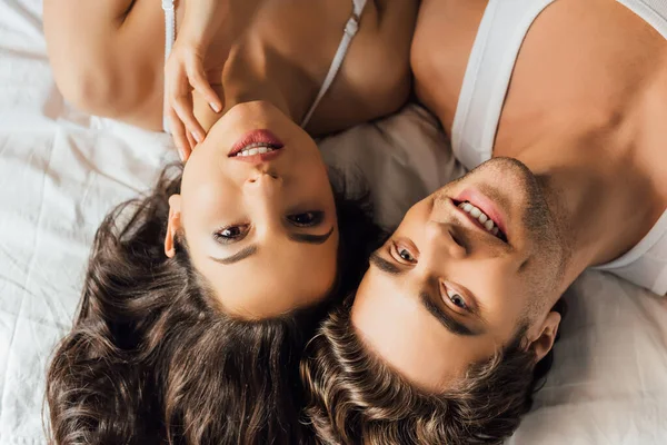 Vue du dessus de l'homme souriant regardant la caméra près de belle femme sur le lit — Photo de stock