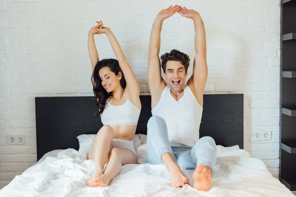 Selective focus of cheerful couple stretching while sitting on bed at morning — Stock Photo