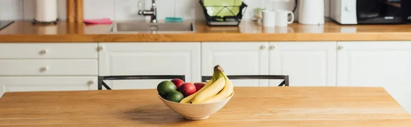 Panoramic shot of fresh fruits in bowl on wooden table in kitchen — Stock Photo
