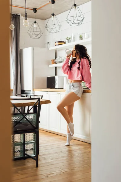 Focus selettivo di una bella donna bruna che beve caffè in cucina — Foto stock