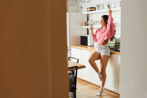 Selektiver Fokus einer fröhlichen Frau, die morgens eine Tasse Kaffee in der Küche hält — Stockfoto