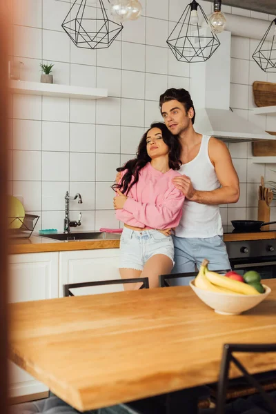 Foco seletivo de homem bonito abraçando bela namorada na cozinha — Fotografia de Stock
