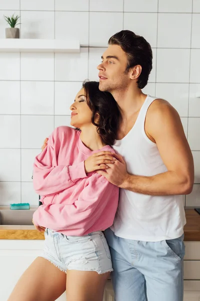 Bonito homem abraçando bela namorada na cozinha — Fotografia de Stock