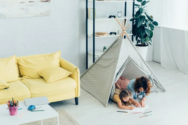High angle view of young nanny and child drawing together while lying in kids wigwam — Stock Photo