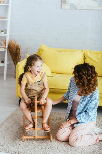 Excited child riding rocking horse near nanny sitting on floor — Stock Photo